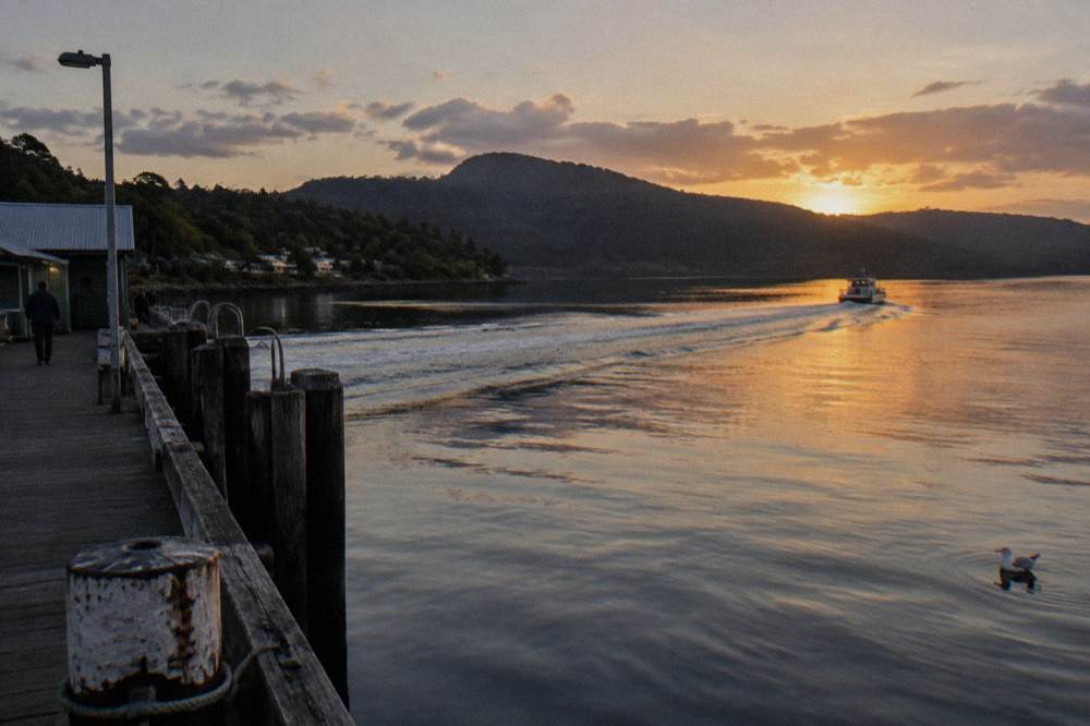 A boat wake crossing dark calm water toward forested hills at dusk