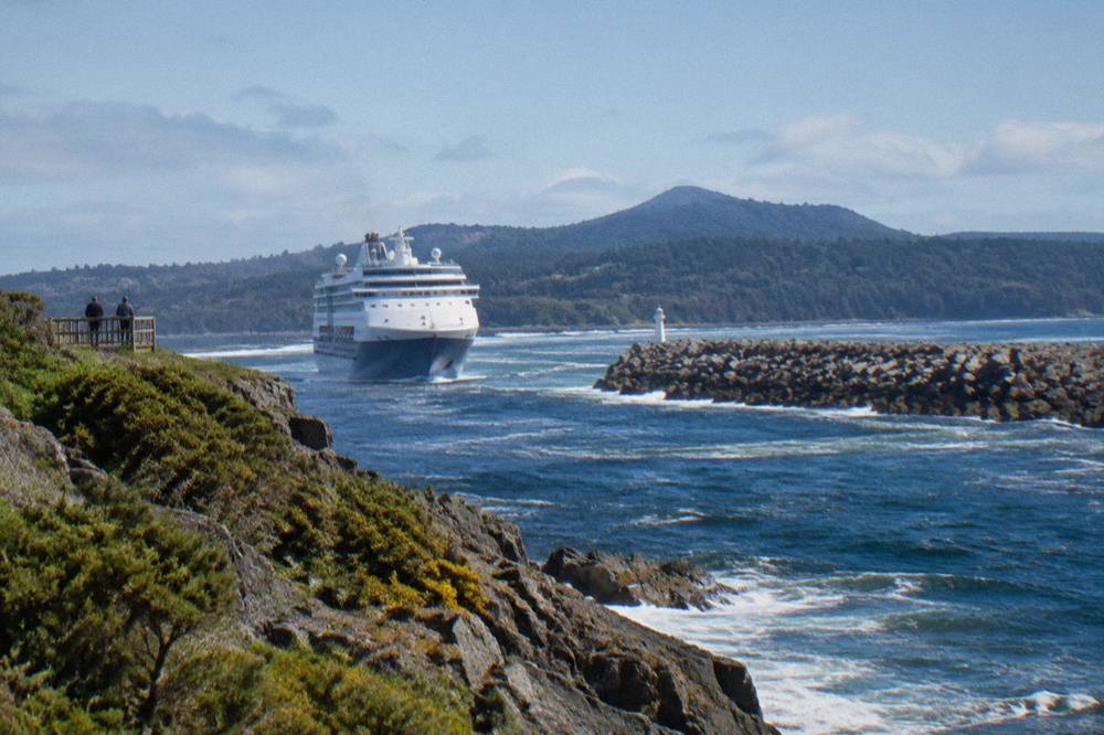 A cruise vessel moving across dark water toward rainforest covered hills on the Gordon River
