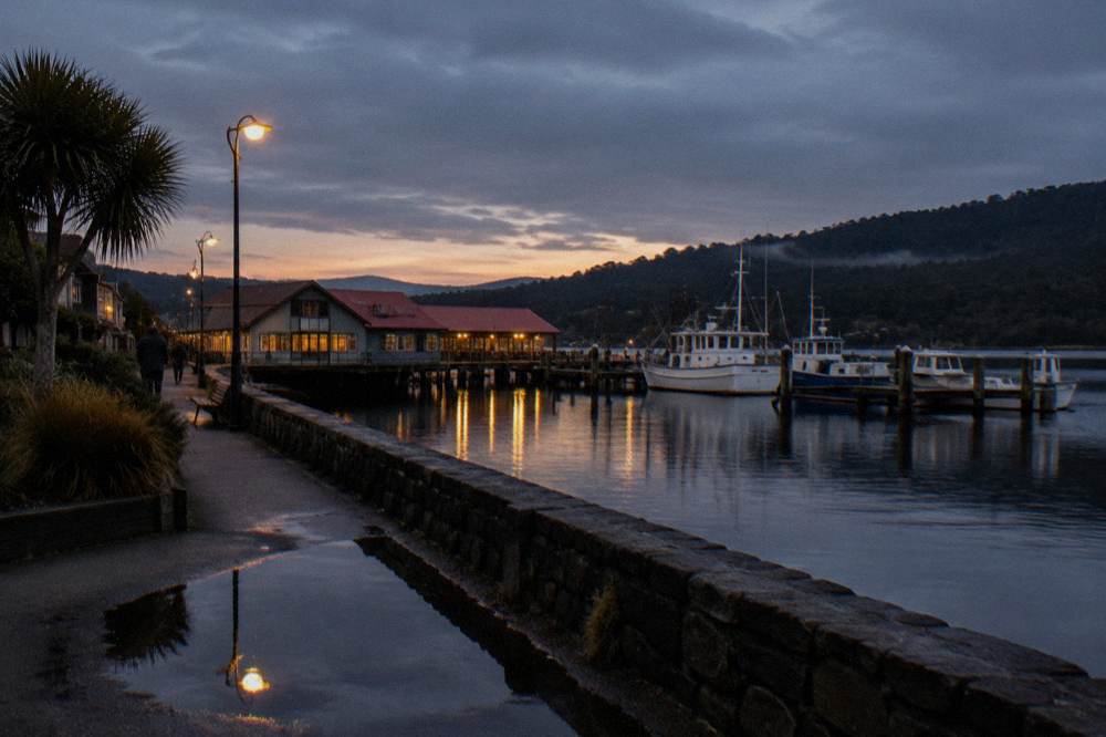 A small waterfront town at dusk with boats moored along a timber wharf