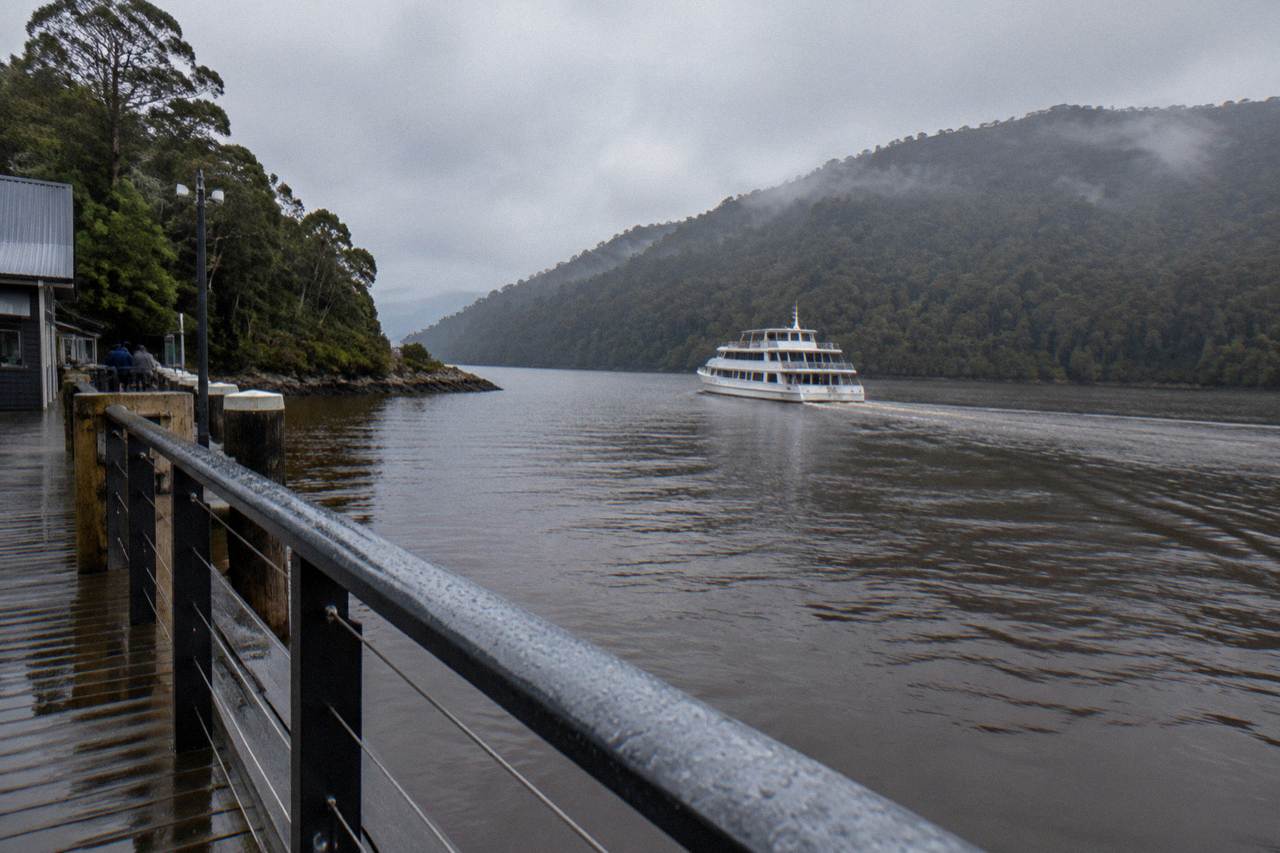A cruise boat on dark tannin-stained water between rainforest hills on the Gordon River in Tasmania