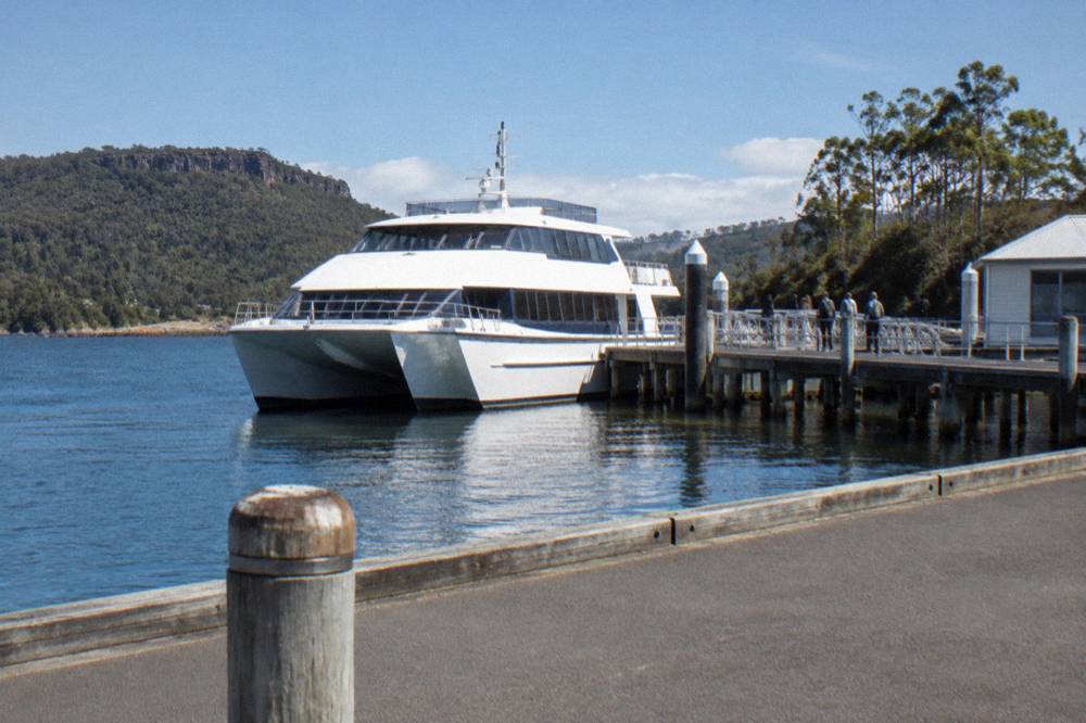 A modern cruise catamaran moored at a wooden wharf on the Strahan waterfront