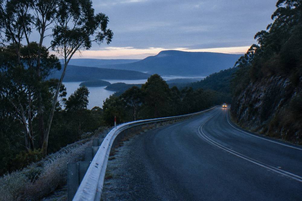 A two-lane highway winding through forested mountains in low light
