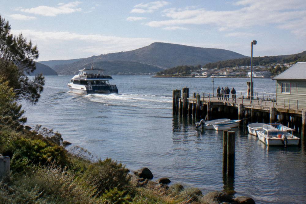 A cruise catamaran pulling away from a small timber wharf into a wide harbour