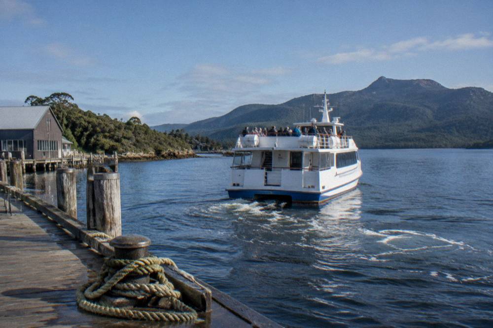 A cruise boat departing a timber wharf in morning light with passengers on deck