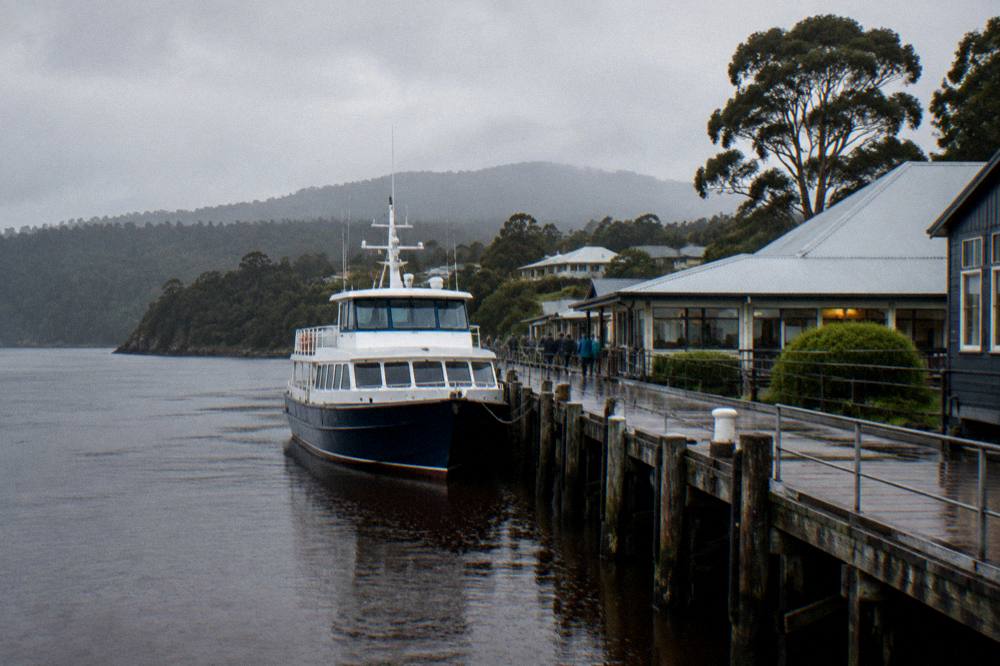 A cruise boat at a wharf in late afternoon light with dark water and distant hills
