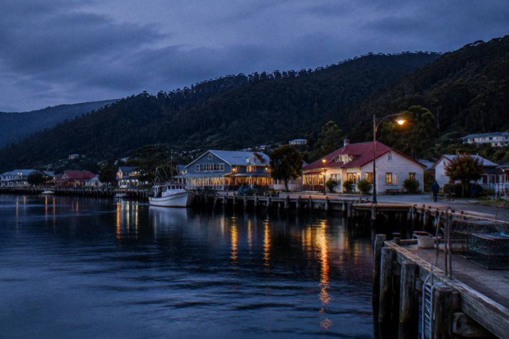 A small west coast fishing town at dusk with a calm harbour and forested hills behind