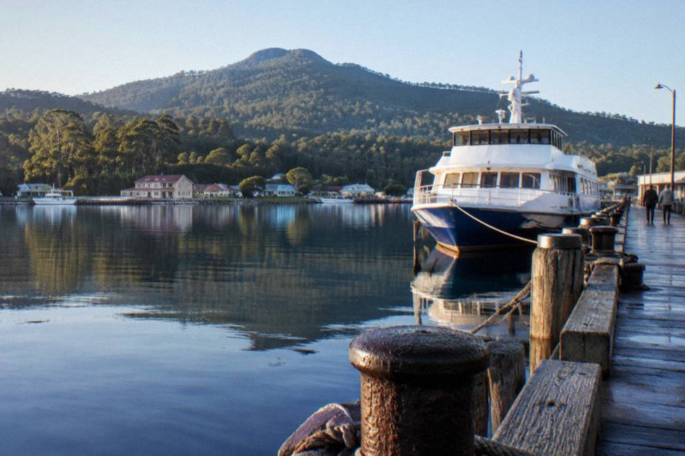 A cruise vessel moored at a timber wharf on a clear morning with forested hills behind