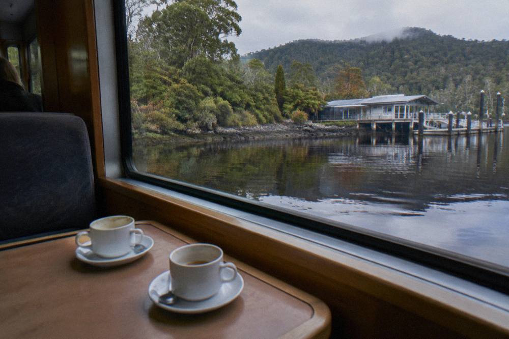 Window table inside a river cruise vessel with dark tannin water and forest reflections outside the glass