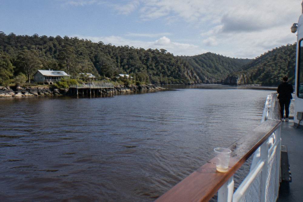 An expanse of dark tea-coloured harbour water with forested low hills on the distant shoreline