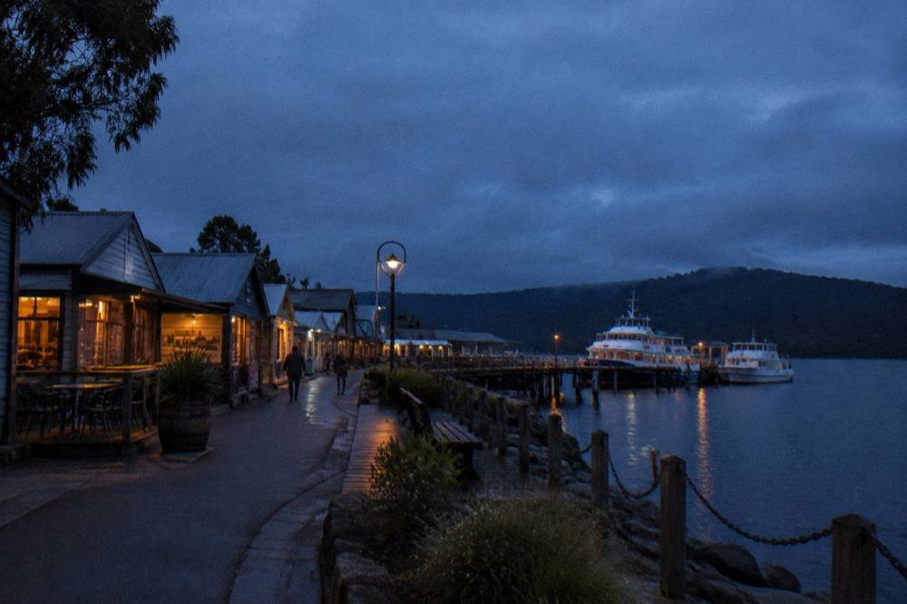 A small waterfront town of low buildings beside a wharf where cruise boats are moored at dusk