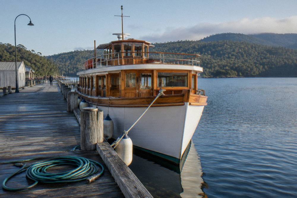 Timber cruise boat tied up at a wharf on a calm harbour, forested hills behind