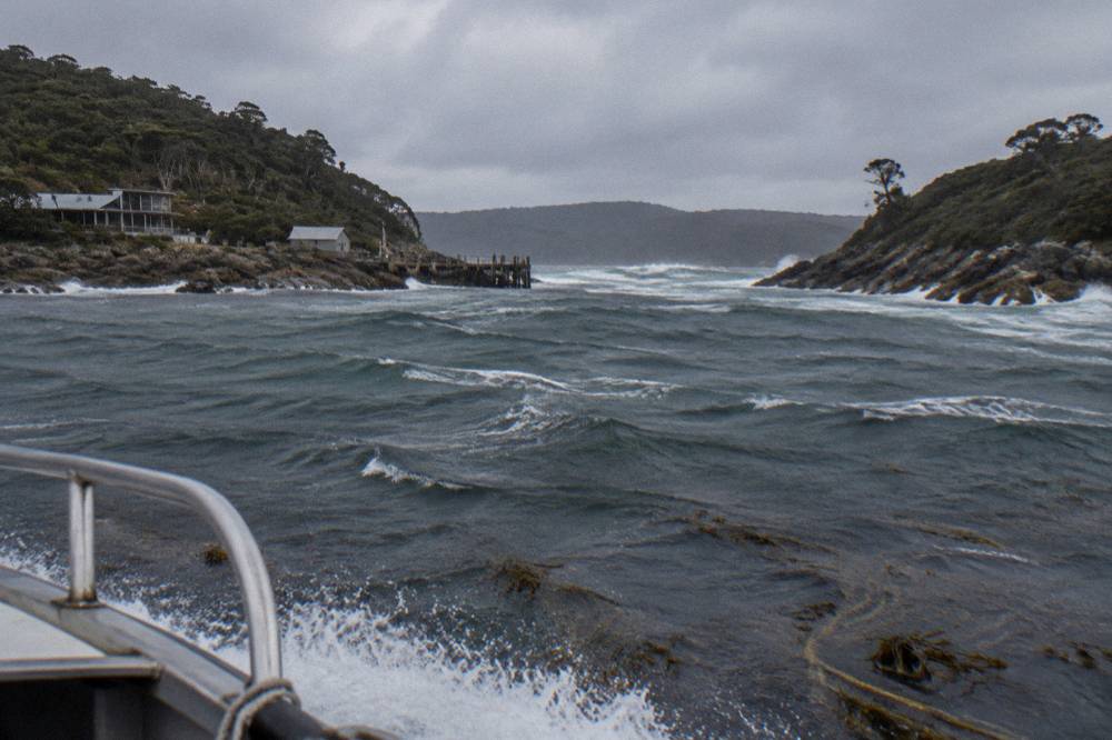Narrow harbour entrance between rocky headlands with ocean swell beyond a shallow channel