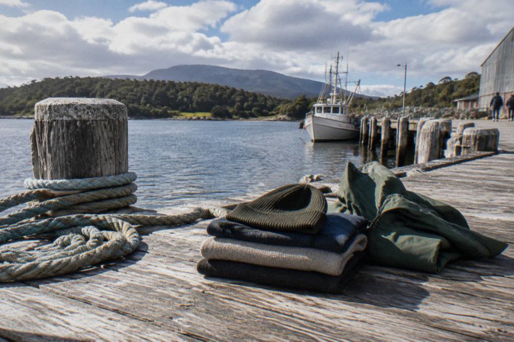 Folded layered clothing with a fleece, rain shell and beanie on a wooden bench
