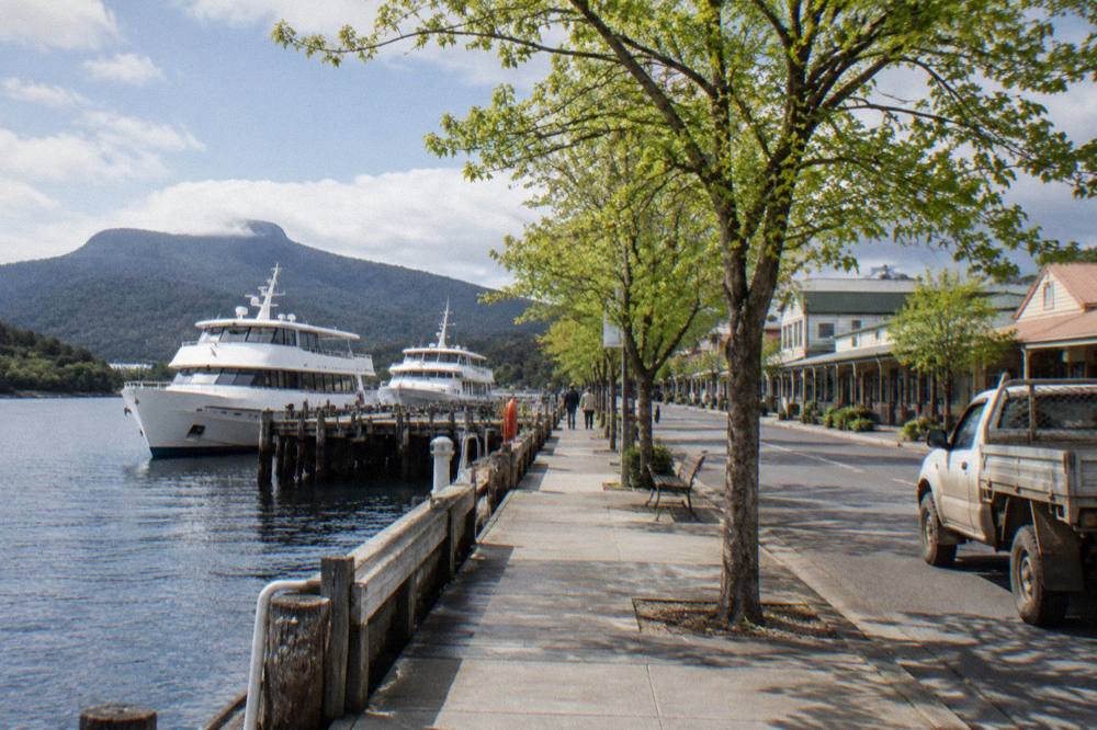 Two cruise vessels moored along a waterfront esplanade with small shops behind them.